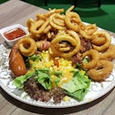 Platter includes bratwurst sausage, calamari, salad, curly fries and banana bacon bites.