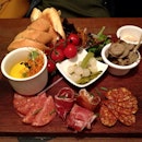 Charcuterie Board: Serrano ham, smoked chorizo, salami, chicken liver & forest mushroom pâté and Cumberland sausage served with pickles, mustard and warm bread